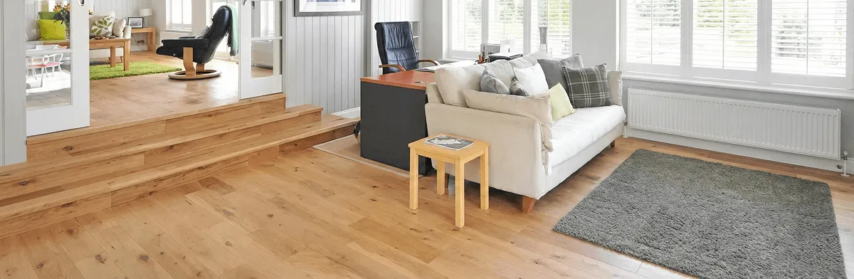 A modern living room with professionally installed laminate flooring, a beige sofa, a small side table, a gray rug, and large windows with white shutters in Evansville, IN